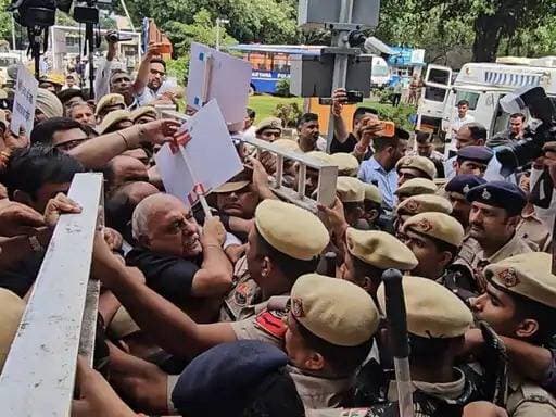 हरियाणा विधानसभा मानसून सेशन में हंगामा- पूर्व सीएम भूपेंद्र सिंह हुड्डा बोले-मुझे गेट पर धक्के मारे,आपने गुंडे भेजे थे क्या?
आज सुबह कांग्रेस के विधायक हाई कोर्ट चौक से काले कपड़े पहनकर विरोध प्रदर्शन करते हुए विधानसभा कूच के लिए निकले थे। विधानसभा के एंट्री गेट के पास पुलिस और सिक्योरिटी ने उन्हें रोक दिया। प्रशासन ने कहा कि विरोध दर्ज करवाते हुए विधायक विधानसभा परिसर में प्रवेश नहीं कर सकते।इस दौरान विधायकों की पुलिस और विधानसभा सिक्योरिटी से बहस हुई और पुलिस ने उनके हाथों से तख्तियां व बैनर छीन लिए। इसके बाद विधायक बैनर छोड़कर नारेबाजी करते हुए विधानसभा परिसर में दाखिल हुए।
#haryanavidhansabha2026