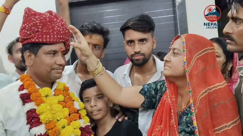 नवनियुक्त सभापति बंशीलाल माली का जोरदार स्वागत, पट्टिका पर लगाया तिलक : जालोर नगर परिषद के सभापति पद पर जीत दर्ज करने के बाद बंशीलाल माली अपने घर पहुंचे। यहां परिजनों, समर्थकों और समाज के लोगों ने उनका जोरदार स्वागत किया। लोगों ने माली को फूलों की माला और साफा पहनाया ओर उनकी मां ने तिलक लगाकर जीत की बधाई दी। इस दौरान उन्हें घी-गुड़ खिलाकर मुंह मीठा कराया गया। समर्थकों ने नवनियुक्त सभापति के नाम की पट्टिका पर भी तिलक लगाकर खुशी जताई। इस दौरान घर पर जश्न का माहौल रहा और बड़ी संख्या में लोगों ने पहुंचकर उन्हें शुभकामनाएं दीं। माली ने सभी का आभार जताते हुए शहर के विकास और जनता की अपेक्षाओं पर खरा उतरने की बात कही।