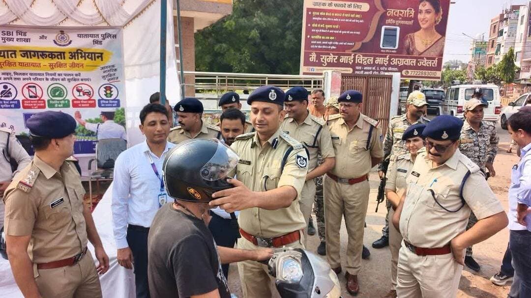 भिण्ड में यातायात जागरूकता कार्यक्रम, पुलिस अधीक्षक ने लोगों को हेलमेट वितरित कर दिया सुरक्षा का संदेश
SBI मुख्य शाखा और यातायात पुलिस की संयुक्त पहल, त्योहारों पर नियमों का पालन करने की अपील
भिण्ड। “सुरक्षित यातायात, सुरक्षित जीवन” अभियान के तहत भारतीय स्टेट बैंक (SBI) की मुख्य शाखा एवं यातायात पुलिस के संयुक्त तत्वावधान में भिण्ड शहर में यातायात जागरूकता कार्यक्रम आयोजित किया गया। कार्यक्रम के दौरान पुलिस अधीक्षक ने आमजन को यातायात नियमों के प्रति जागरूक करते हुए दोपहिया वाहन चालकों को हेलमेट पहनने की समझाइश दी। साथ ही, हेलमेट वितरित कर लोगों को सड़क सुरक्षा का संदेश दिया गया।
कार्यक्रम में पुलिस अधीक्षक ने कहा कि सड़क पर वाहन चलाते समय सावधानी बरतना और यातायात नियमों का पालन करना प्रत्येक नागरिक की जिम्मेदारी है। दोपहिया वाहन चालकों को हमेशा हेलमेट पहनकर ही वाहन चलाना चाहिए, जबकि चारपहिया वाहन चालकों को सीट बेल्ट का अनिवार्य रूप से उपयोग करना चाहिए।
त्योहारों पर सतर्कता बरतने की अपील
आगामी त्योहारों को देखते हुए भिण्ड पुलिस ने आमजन से यातायात नियमों का पालन करने की अपील की है। पुलिस ने निर्धारित गति सीमा में वाहन चलाने, वाहन चलाते समय सावधानी बरतने तथा अपनी और दूसरों की सुरक्षा का ध्यान रखने की बात कही।
पुलिस के अनुसार, यातायात नियमों का पालन केवल चालानी कार्रवाई से बचने के लिए ही नहीं, बल्कि सड़क दुर्घटनाओं की आशंका कम करने और अनमोल जीवन की रक्षा करने के लिए भी जरूरी है।
भिण्ड पुलिस का संदेश
भिण्ड पुलिस ने नागरिकों से अपील की है कि वे यातायात नियमों का पालन करें, दोपहिया वाहन चलाते समय हेलमेट और चारपहिया वाहन चलाते समय सीट बेल्ट का उपयोग करें। जिम्मेदार नागरिक बनें और स्वयं के साथ दूसरों का जीवन भी सुरक्षित रखें।
संदेश साफ है—सुरक्षा अपनाएं, यातायात नियमों का पालन करें और सुरक्षित घर पहुंचें।